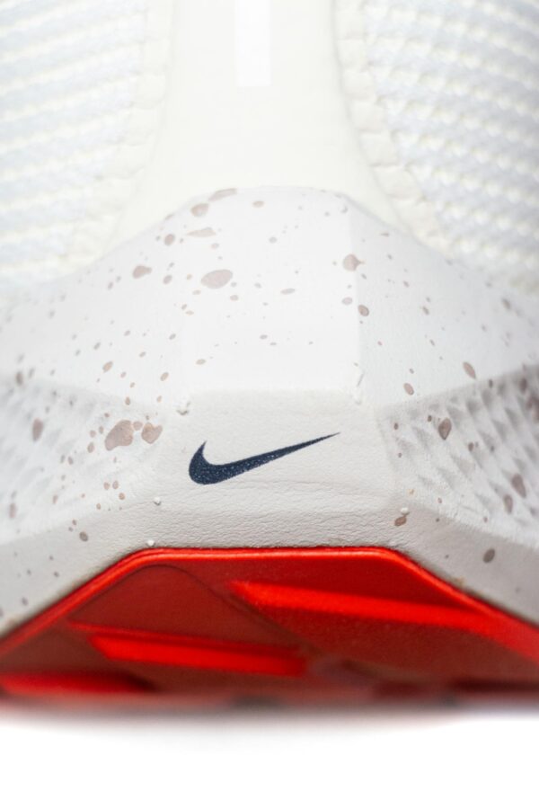Detailed view of a white sneaker featuring speckled design and red sole.