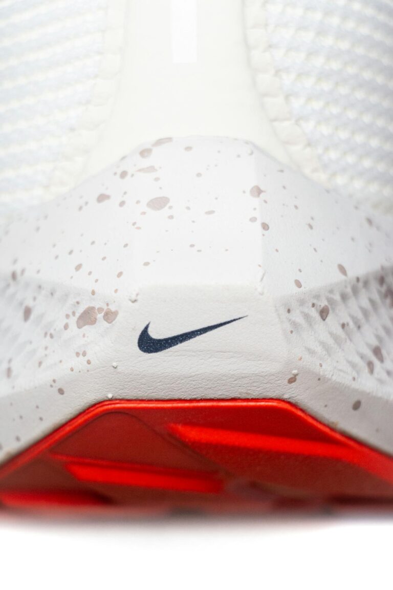 Detailed view of a white sneaker featuring speckled design and red sole.
