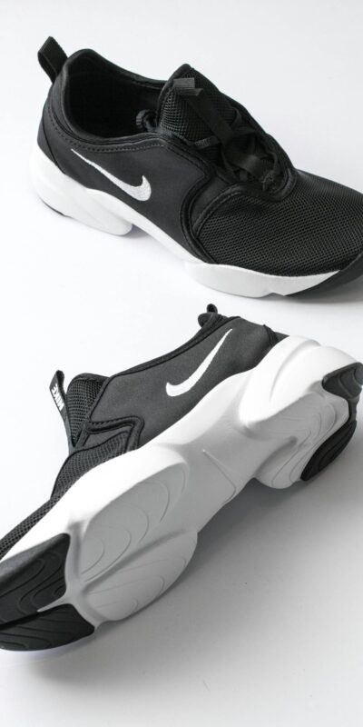 From above of sports shoes pair with black breathable surface and white soles comfortable suiting on feet placed on white background