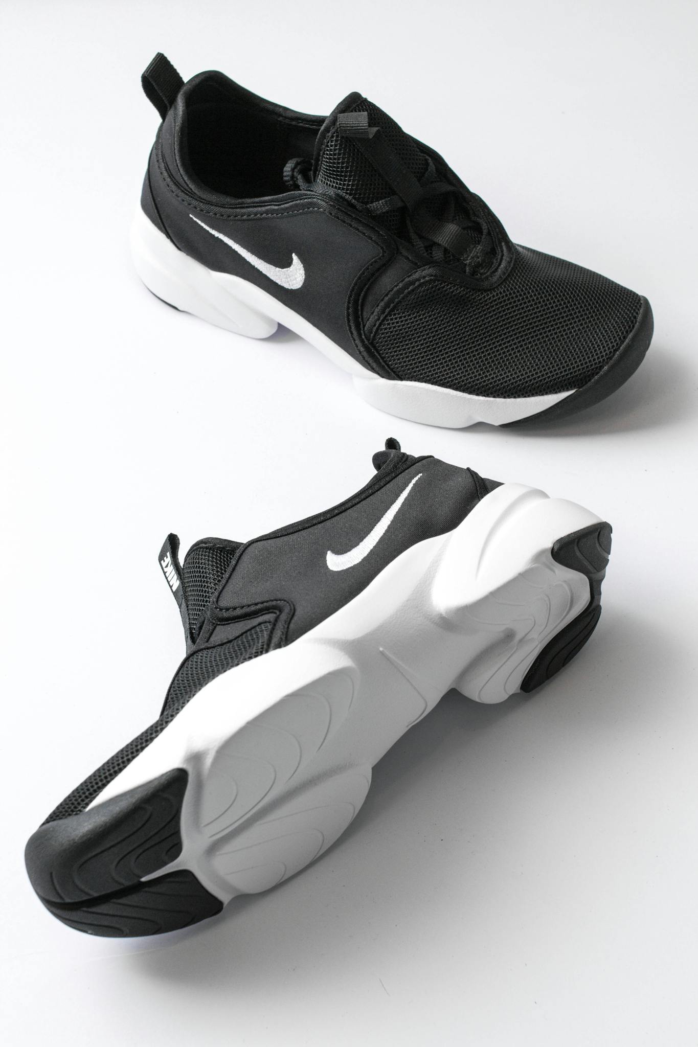 From above of sports shoes pair with black breathable surface and white soles comfortable suiting on feet placed on white background